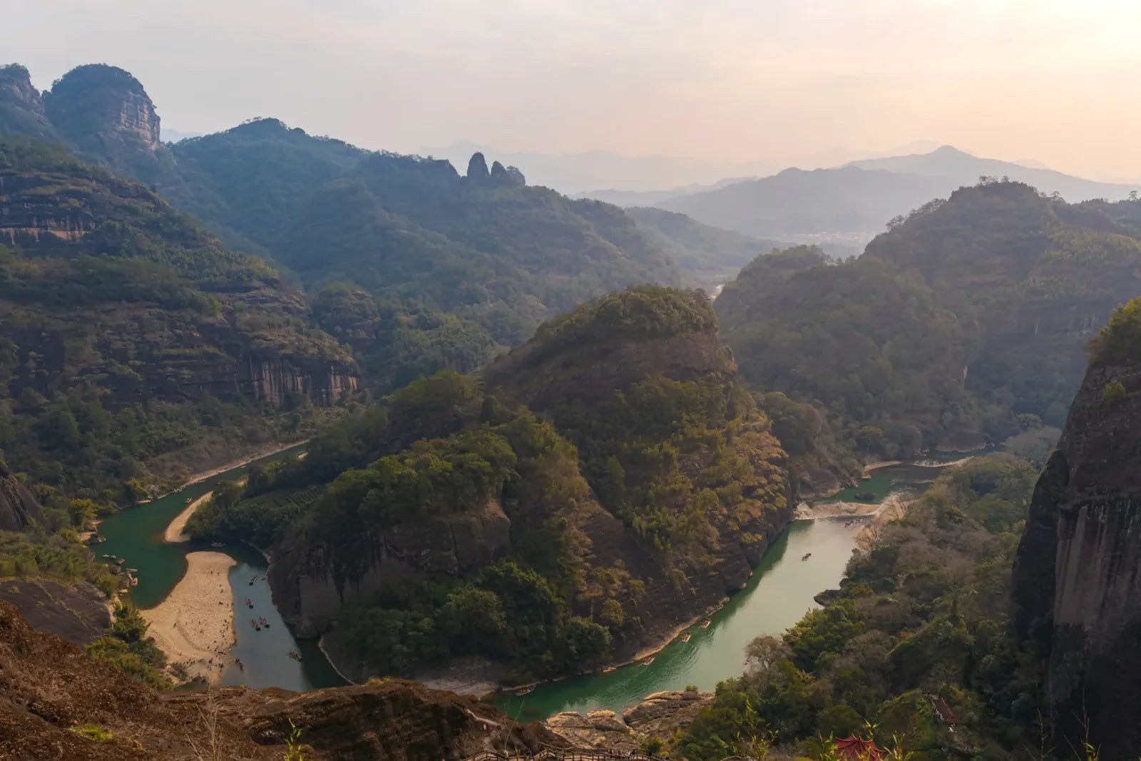 Iconic Wuyi Mountains landscape with steep red cliffs, emerald river bend and misty terraced hills