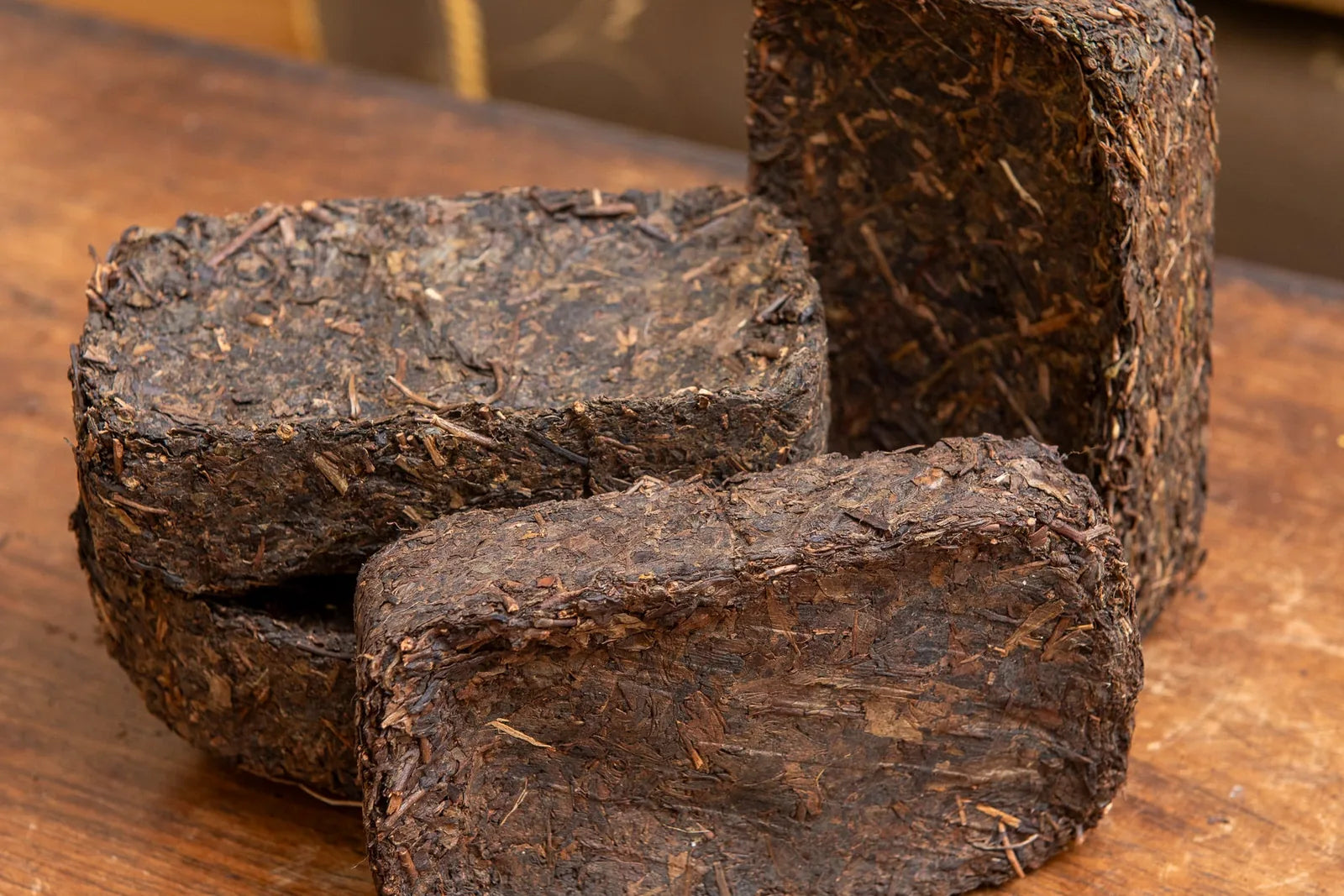 Three stacked compressed dark hei cha tea bricks on wood showing coarse stems and dark leaves