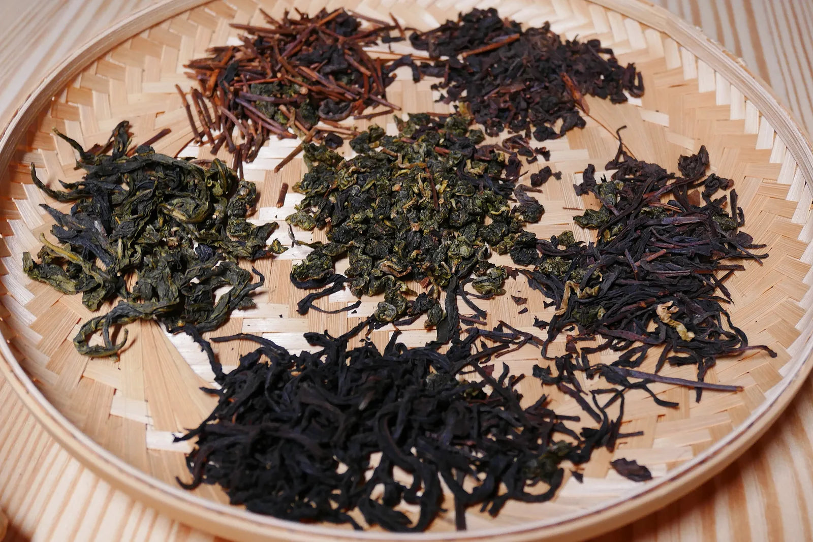 Six varieties of Taiwanese tea leaves arranged on a bamboo tray showing oolong, black and green styles